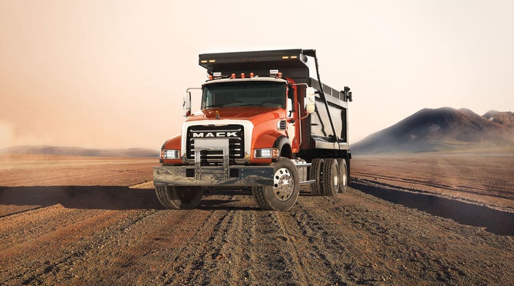 Front view of a red Mack Granite dump truck on a dirt site, showcasing its robust grille and large dump bed