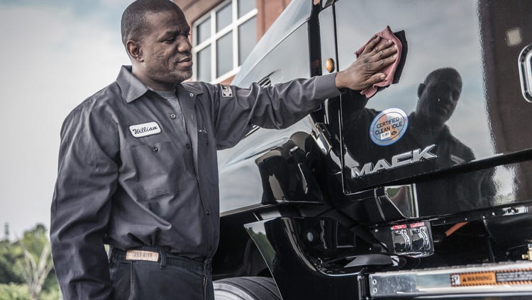 Mack technician cleaning the side of a truck cab with a 'Certified Clean Idle' sticker