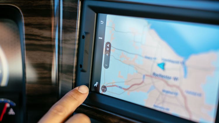Close-up of a Mack truck's touchscreen navigation system displaying a map, with a hand selecting an option