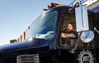 A driver behind the wheel of a black Mack truck.