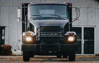 Front view of a black Mack MD Series truck parked in front of a business.